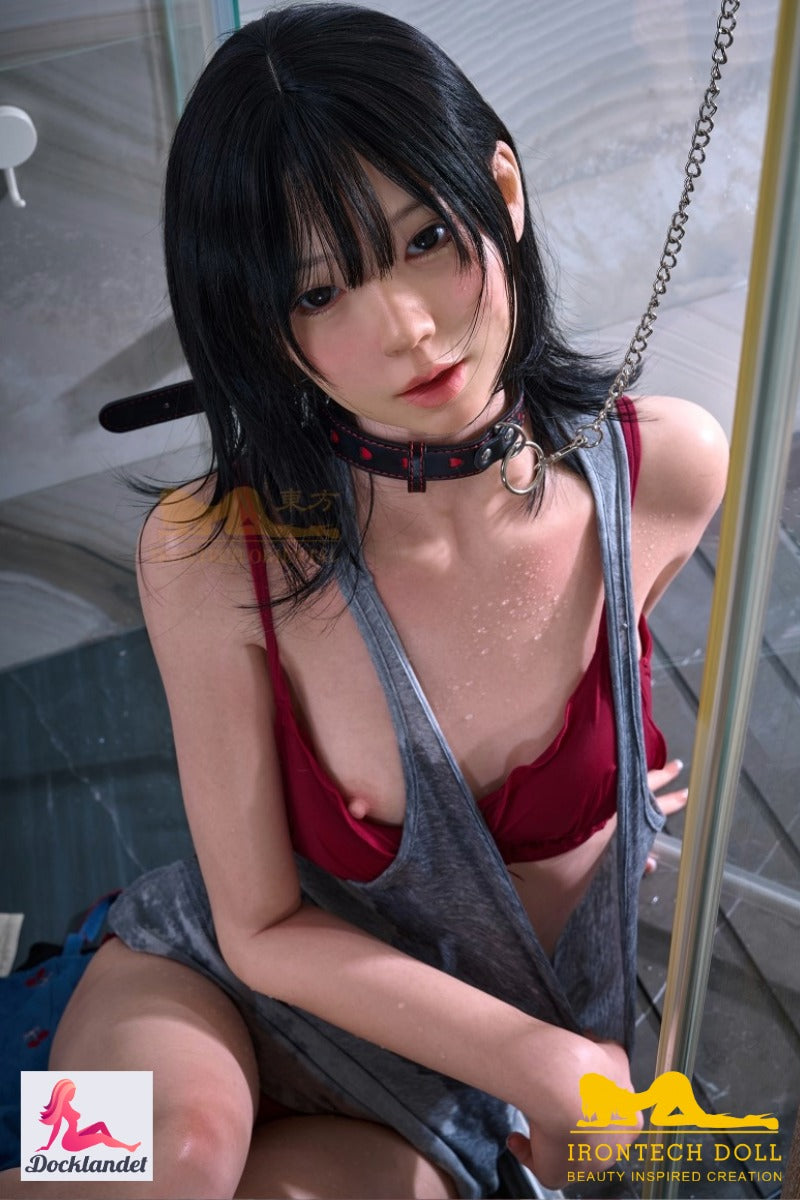 Verdzības seksa lelle Kurumi no Irontech Doll, sēžu dušā ar melniem matiem, sarkanu bikini un slapji pelēku topiņu, tuvplāns vannasistabas vidē.