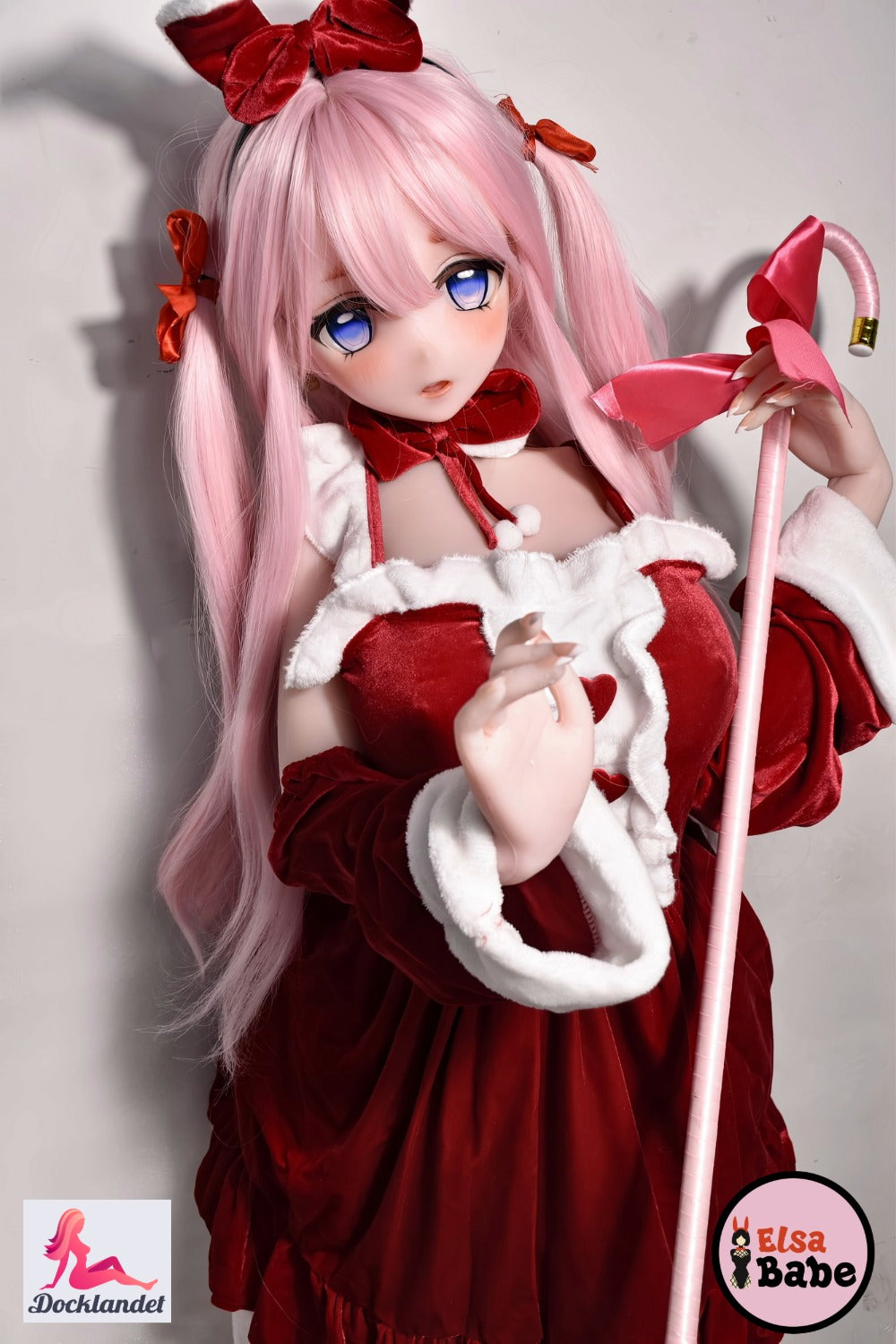 ElsaBabe Itsuki Sango 148 cm anime waifu lelle, valkā sarkanbaltu Ziemassvētku kleitu ar bantēm, rozā matiem un zilām acīm, tur rozā zizli ar lielu banti.